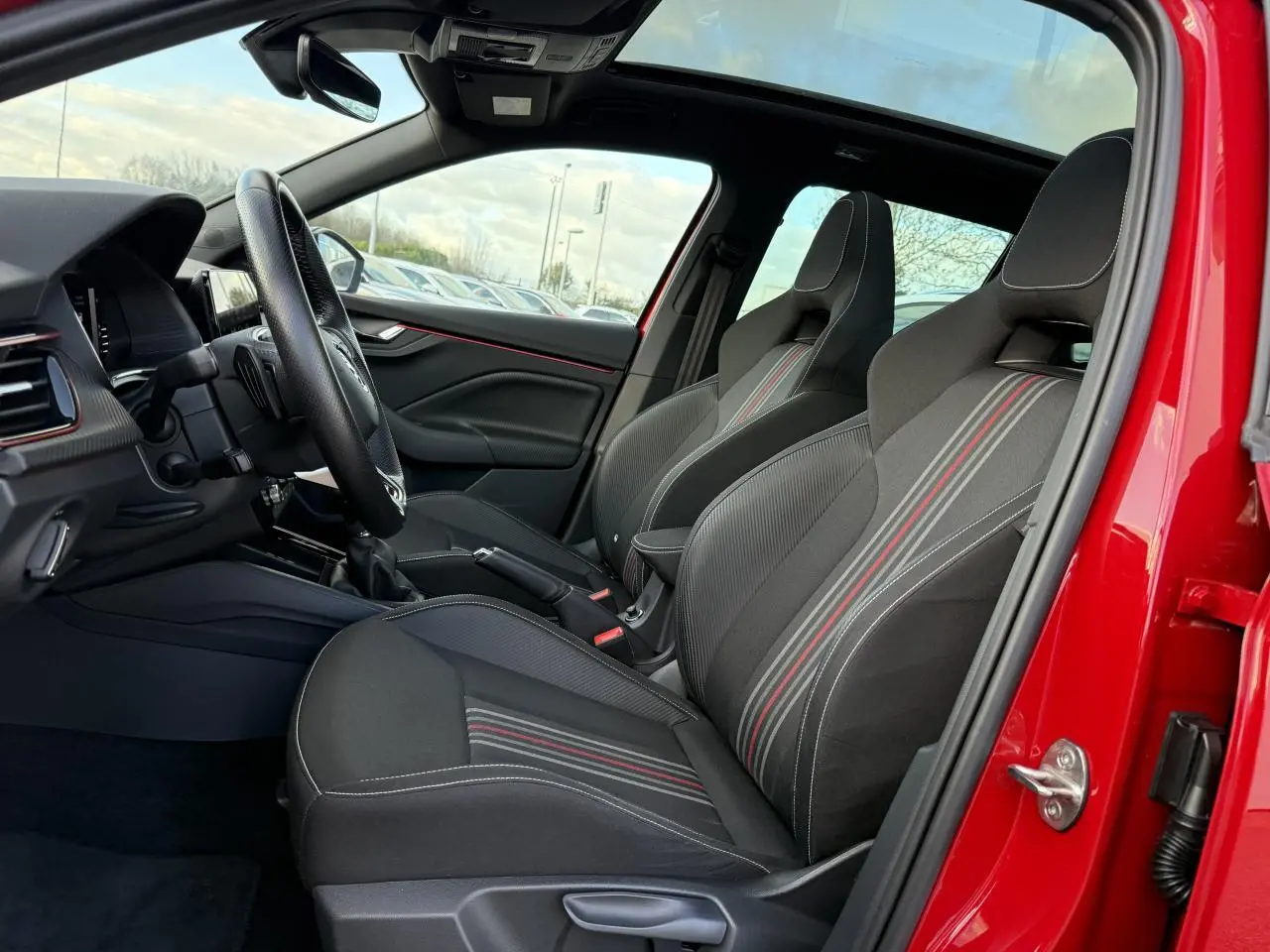 Vue intérieure côté gauche du Skoda Kamiq rouge velvet, sièges sport noirs avec bandes rouges et volant cuir multifonctions.