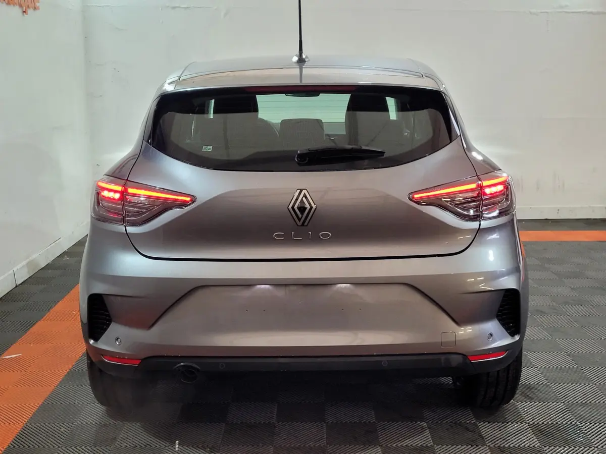 Vue arrière d'une Renault Clio gris foncé 2025 avec feux LED allumés, dans un garage au sol carrelé noir et orange.