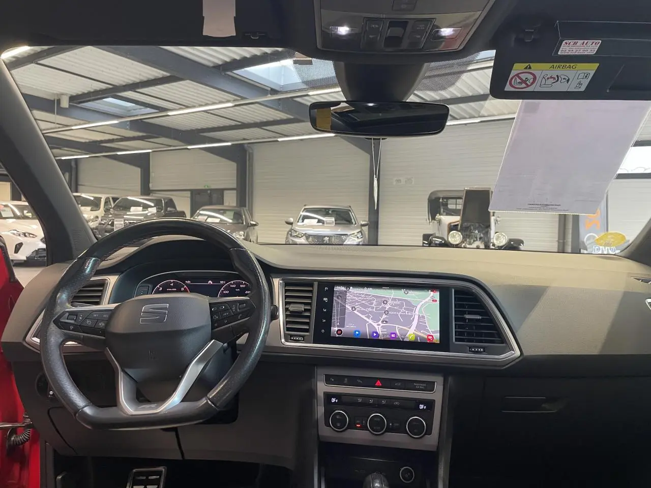 Vue intérieure frontale du tableau de bord du SEAT Ateca rouge 2022, avec écran tactile de navigation et volant multifonction.