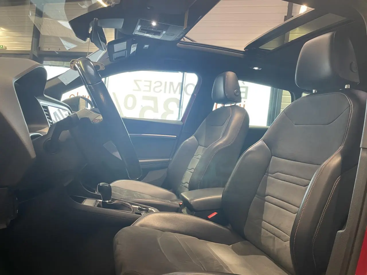 Intérieur du SEAT Ateca 2022 rouge, vue côté conducteur, sièges sport noirs avec surpiqûres contrastées et toit ouvrant.