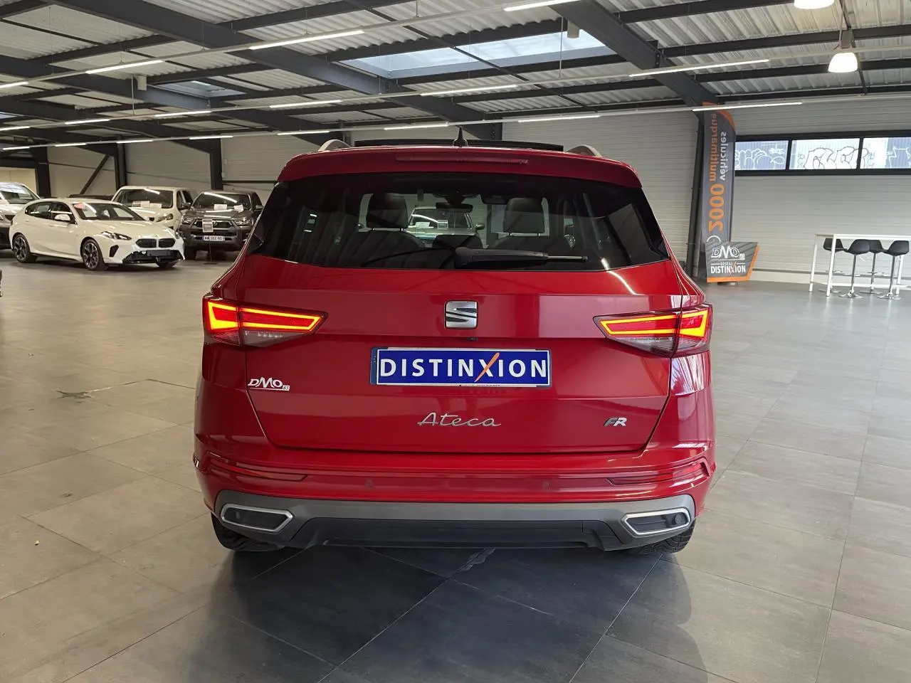 Vue arrière d'un SEAT Ateca rouge 2022 en finition FR, avec feux allumés dans un showroom lumineux.