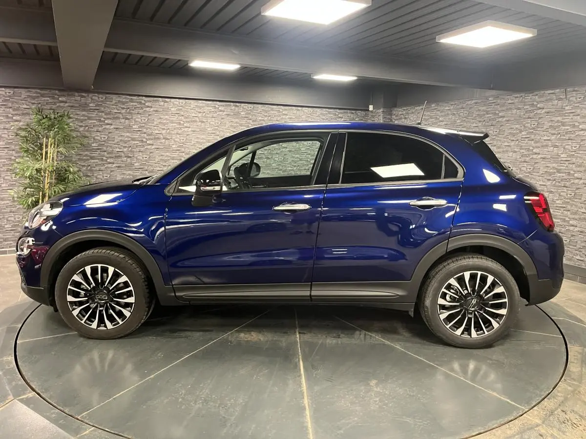 Profil latéral droit d'une Fiat 500X bleu métallisé avec jantes alliage 17 pouces dans un showroom.