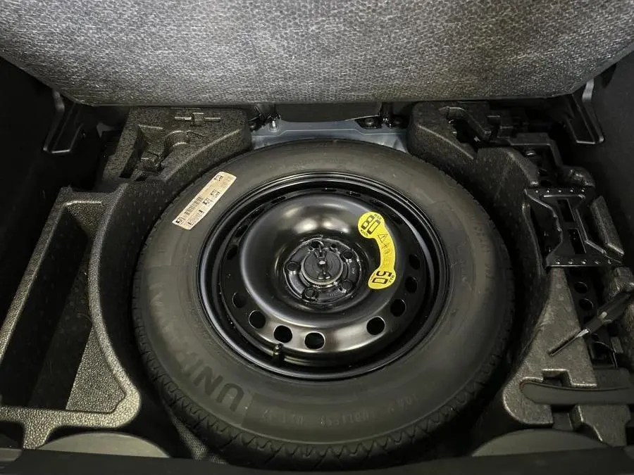 Vue en plongée sur la roue de secours noire dans le coffre d'une Fiat 500X bleu 2024.