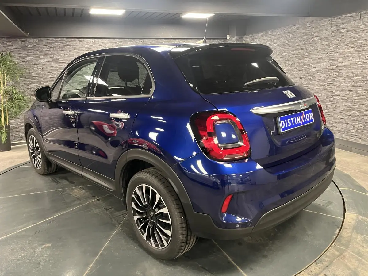 Vue 3/4 arrière droite d'un Fiat 500X bleu métallisé avec jantes alliage 17'' et vitres surteintées.