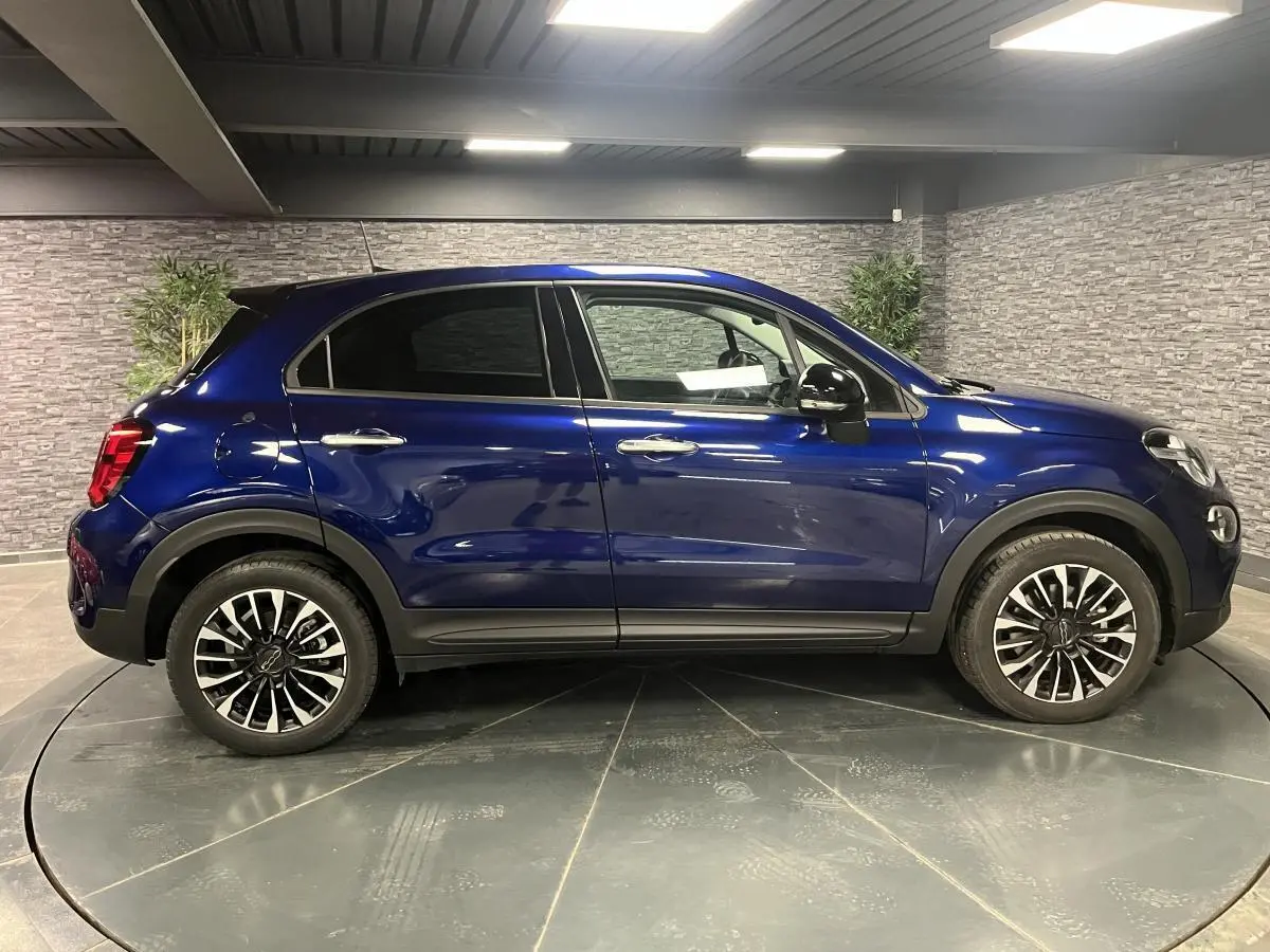 Vue de profil côté gauche d'un Fiat 500X bleu métallisé avec jantes alliage 17 pouces dans un showroom.