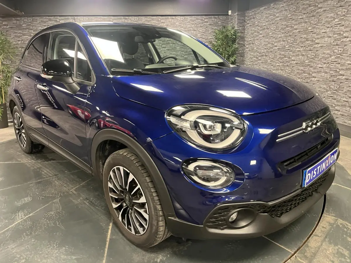 Fiat 500X bleu métallisé vue 3/4 avant droit avec jantes alliage 17'' et phares LED dans un showroom.