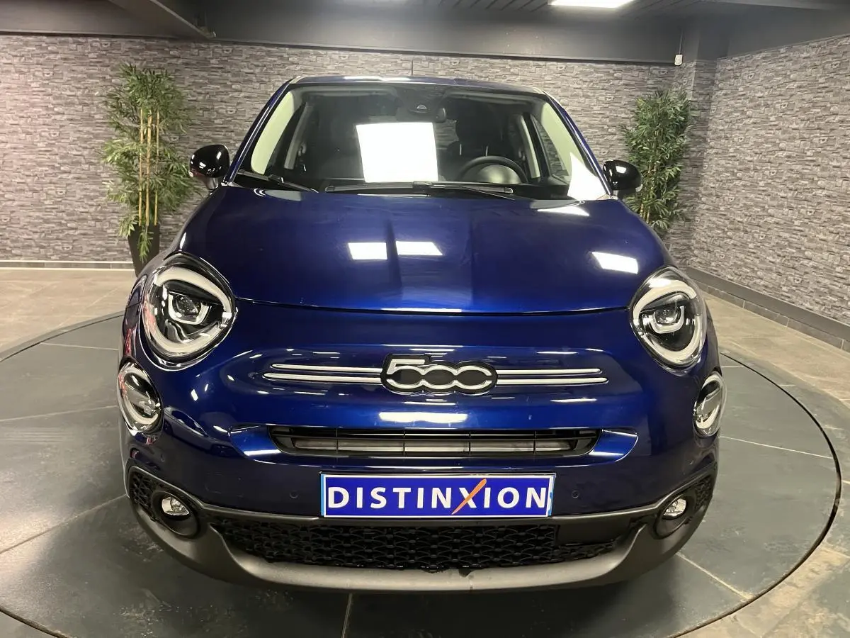 Vue frontale d'une Fiat 500X bleu métallisé avec logo 500 distinctif et phares LED dans un showroom.