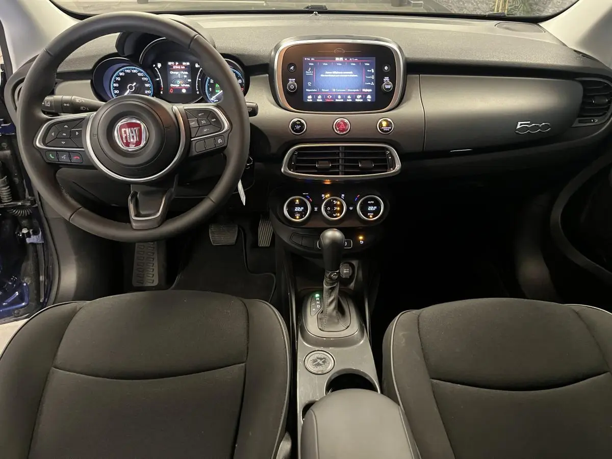 Intérieur de la Fiat 500X 2024 bleu, vue de face sur le tableau de bord avec écran tactile et volant multifonction.