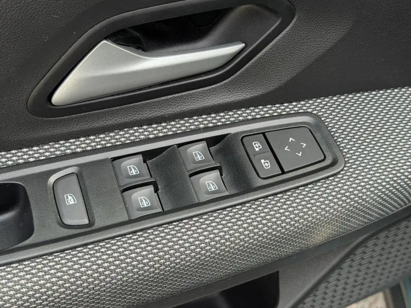 Gros plan sur la commande des vitres électriques et rétroviseurs côté conducteur du Dacia Jogger 2025, tissu gris texturé visible.