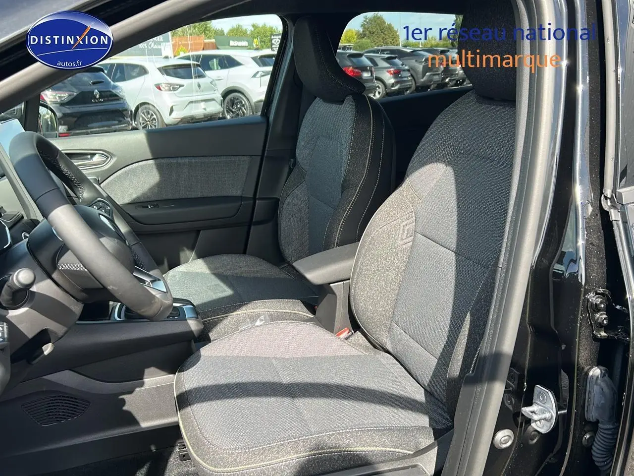 Vue intérieure côté conducteur du Renault Captur noir étoile 2025, mettant en valeur les sièges tissu et l'accoudoir central.