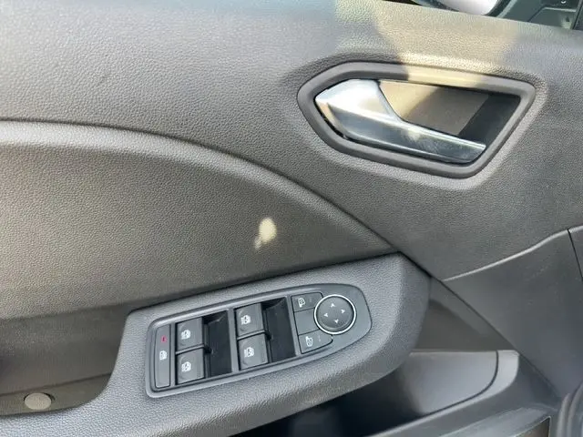 Détail de la porte côté conducteur de la Renault Clio blanche 2025, avec commandes électriques des vitres et poignée intérieure chromée.