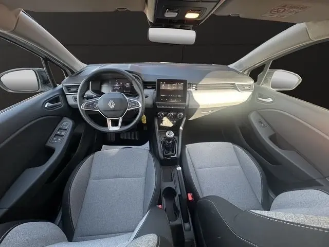 Vue intérieure avant de la Renault Clio blanche 2025, volant multifonctions, écran tactile central et sièges gris clair.