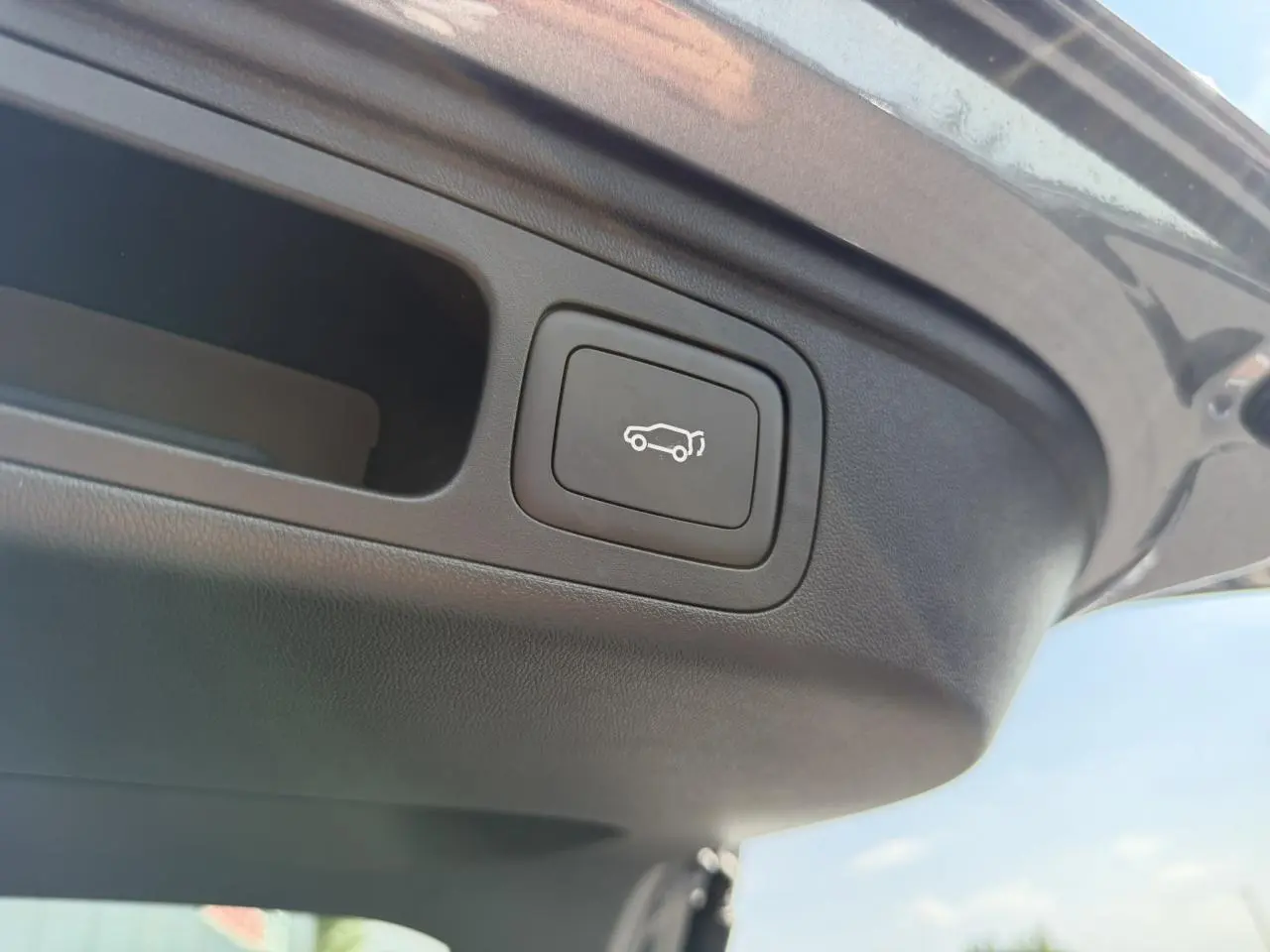 Bouton d'ouverture électrique du hayon sur le bord intérieur du coffre d'un MG Motor EHS gris métallisé.