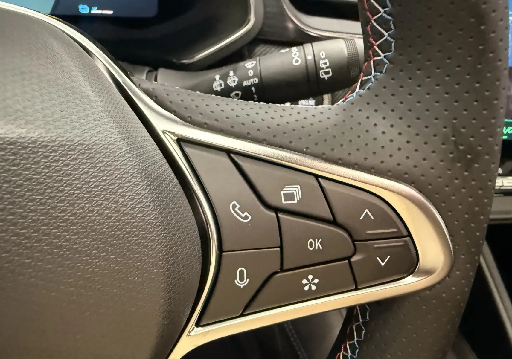 Gros plan sur les commandes multifonctions côté gauche du volant perforé avec surpiqûres tricolores du Renault Symbioz gris Rafale.