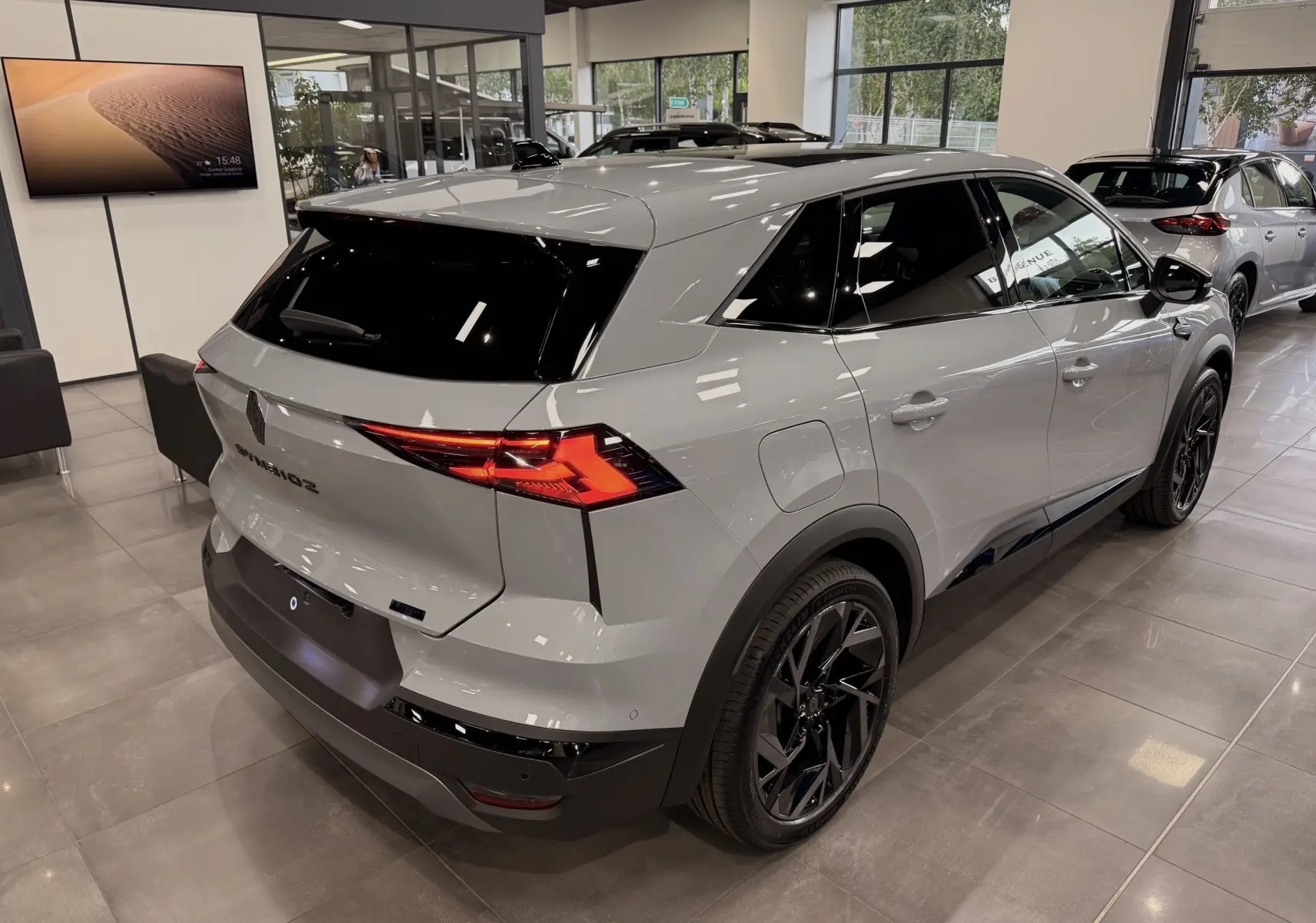 Vue 3/4 arrière droite du Renault SYMBIOZ gris Rafale en showroom, avec jantes noires et vitres teintées.