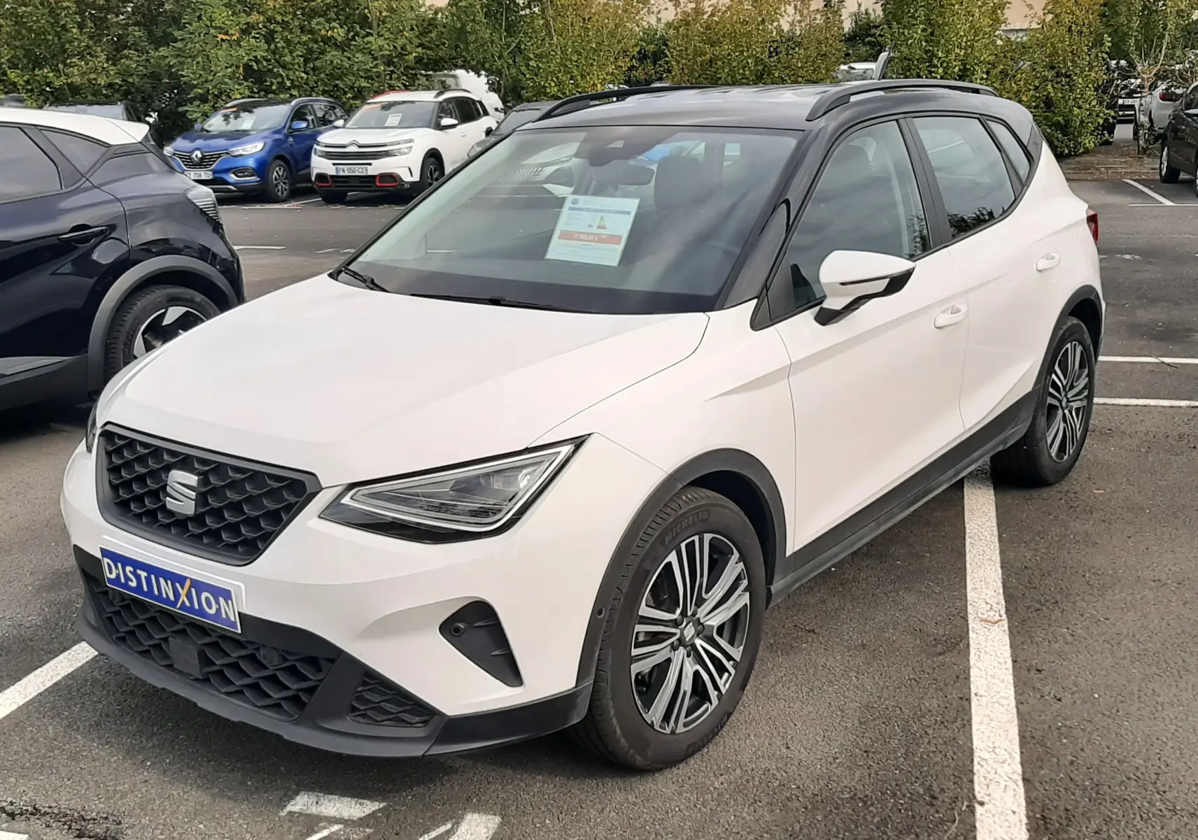 SEAT Arona blanc avec toit noir, vue 3/4 avant droit, stationné sur un parking extérieur.