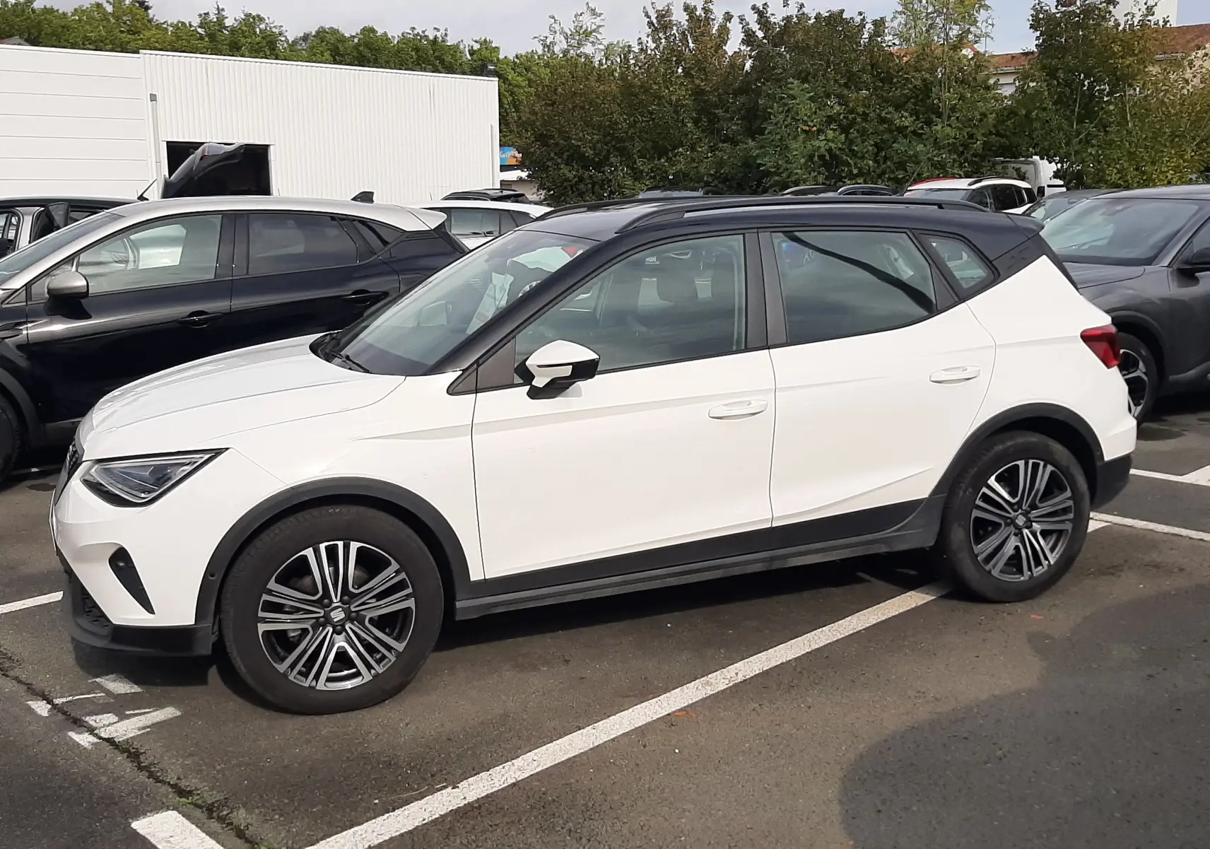 SEAT Arona 2024 blanc avec toit noir, vue de profil côté gauche, roues alliage et lignes modernes.