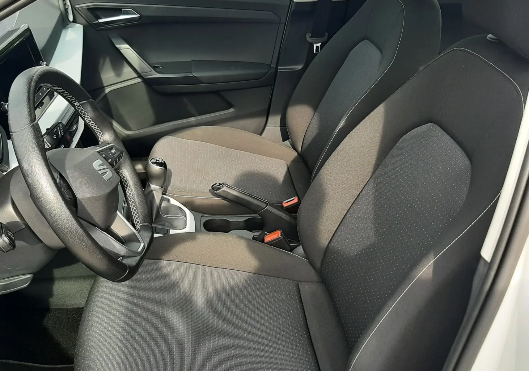 Vue intérieure côté conducteur du SEAT Arona blanc 2024, montrant les sièges noirs en tissu et le volant multifonction.