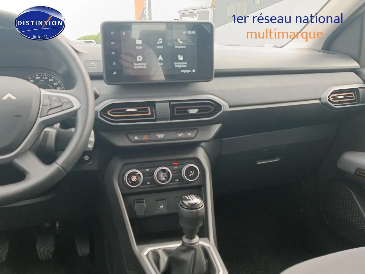 Vue intérieure côté conducteur du tableau de bord noir de la Dacia Sandero 2025 avec écran tactile et levier de vitesse manuel.