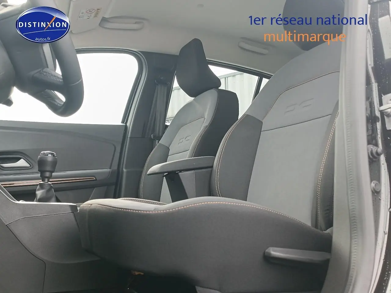 Vue intérieure côté gauche montrant les sièges avant noirs avec accoudoir central de la Dacia Sandero Stepway 2025.