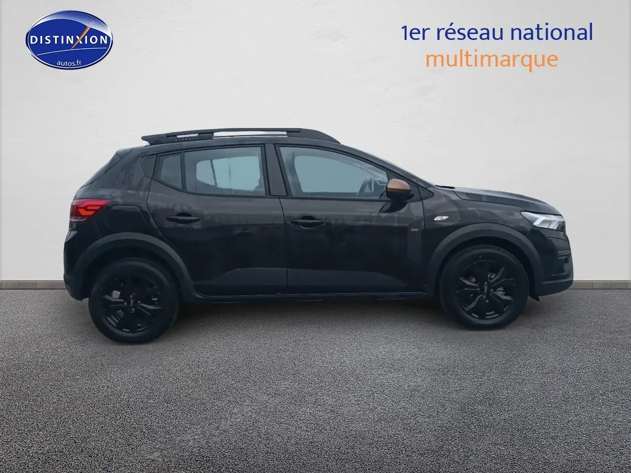 Profil côté gauche de la Dacia Sandero Stepway noire 2025 avec barres de toit et jantes alu noires.