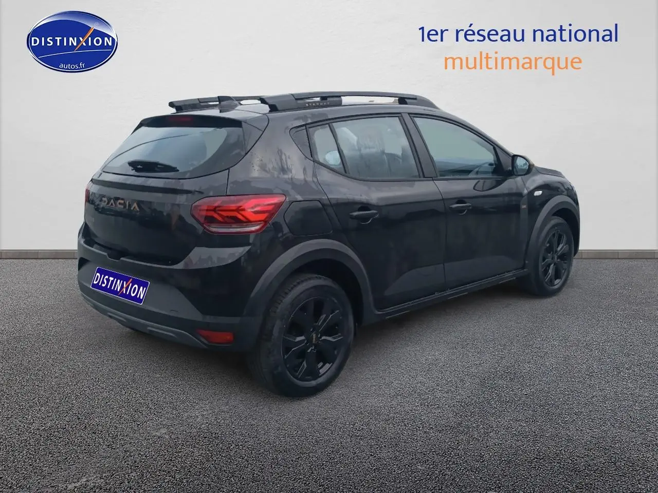 Vue 3/4 arrière droite d'une Dacia Sandero noire avec barres de toit et jantes noires sur fond neutre.