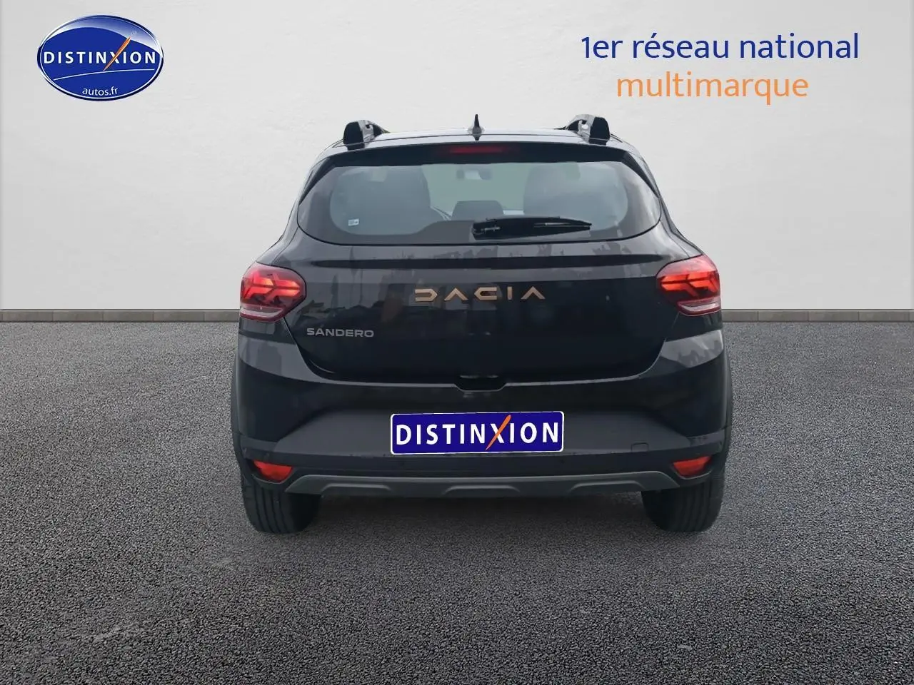 Vue arrière d'une Dacia Sandero noire 2025 avec feux arrière allumés et logo DACIA en relief cuivré.