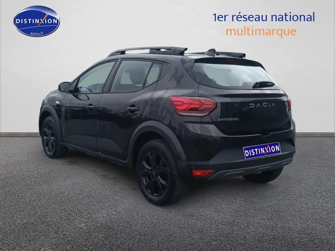 Vue 3/4 arrière droite d'une Dacia Sandero noire avec barres de toit et jantes alu noires.