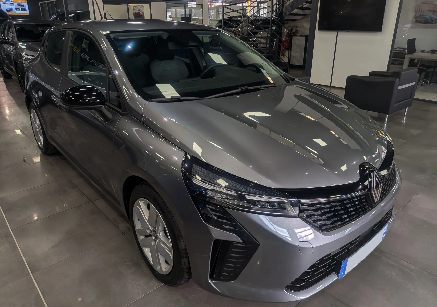 Renault Clio V TCe 90 Evolution gris schiste vue 3/4 avant en showroom avec phares LED et calandre noire.