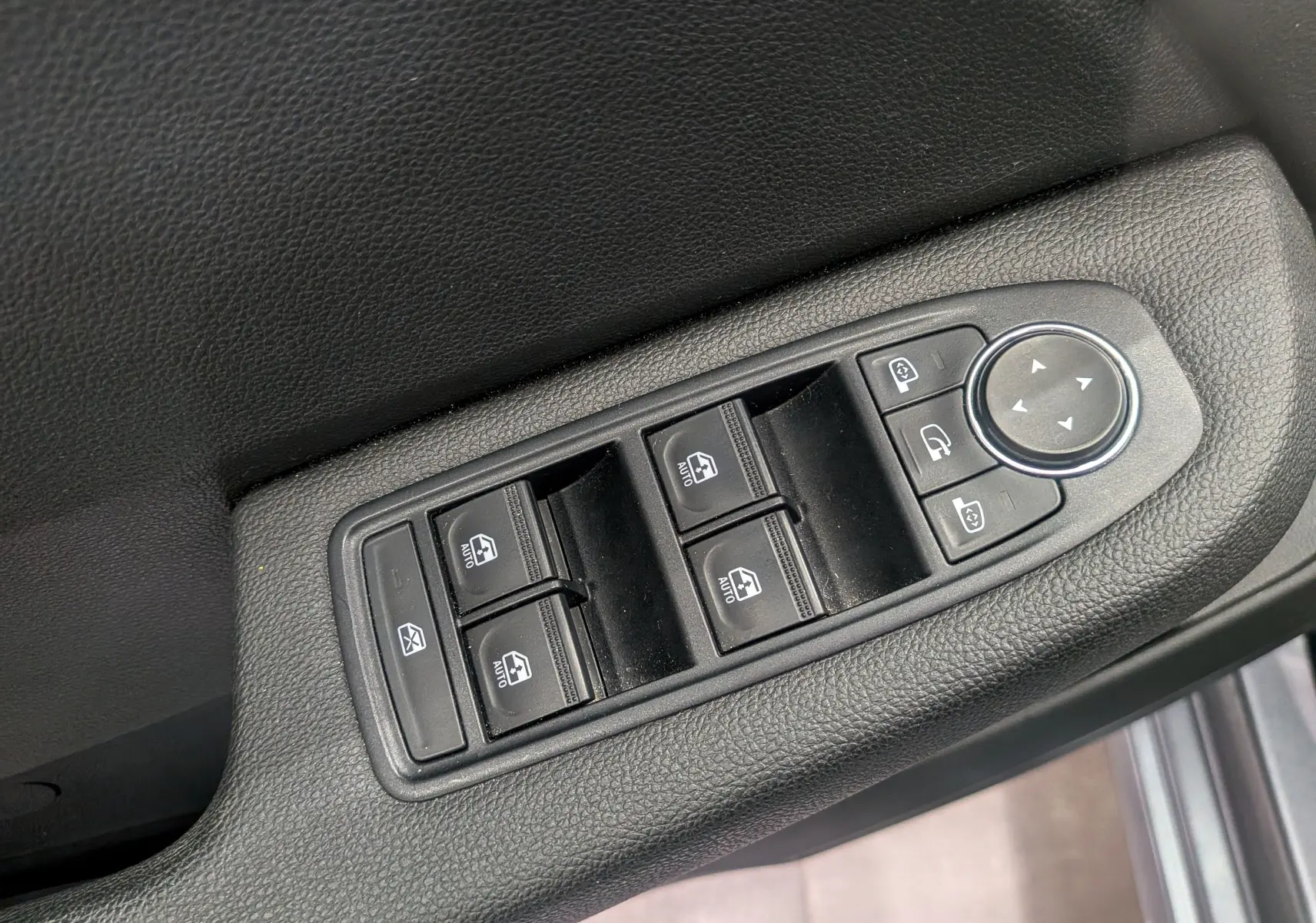 Gros plan sur les commandes de lève-vitres et réglage des rétroviseurs côté conducteur d’une Renault Clio V gris schiste.