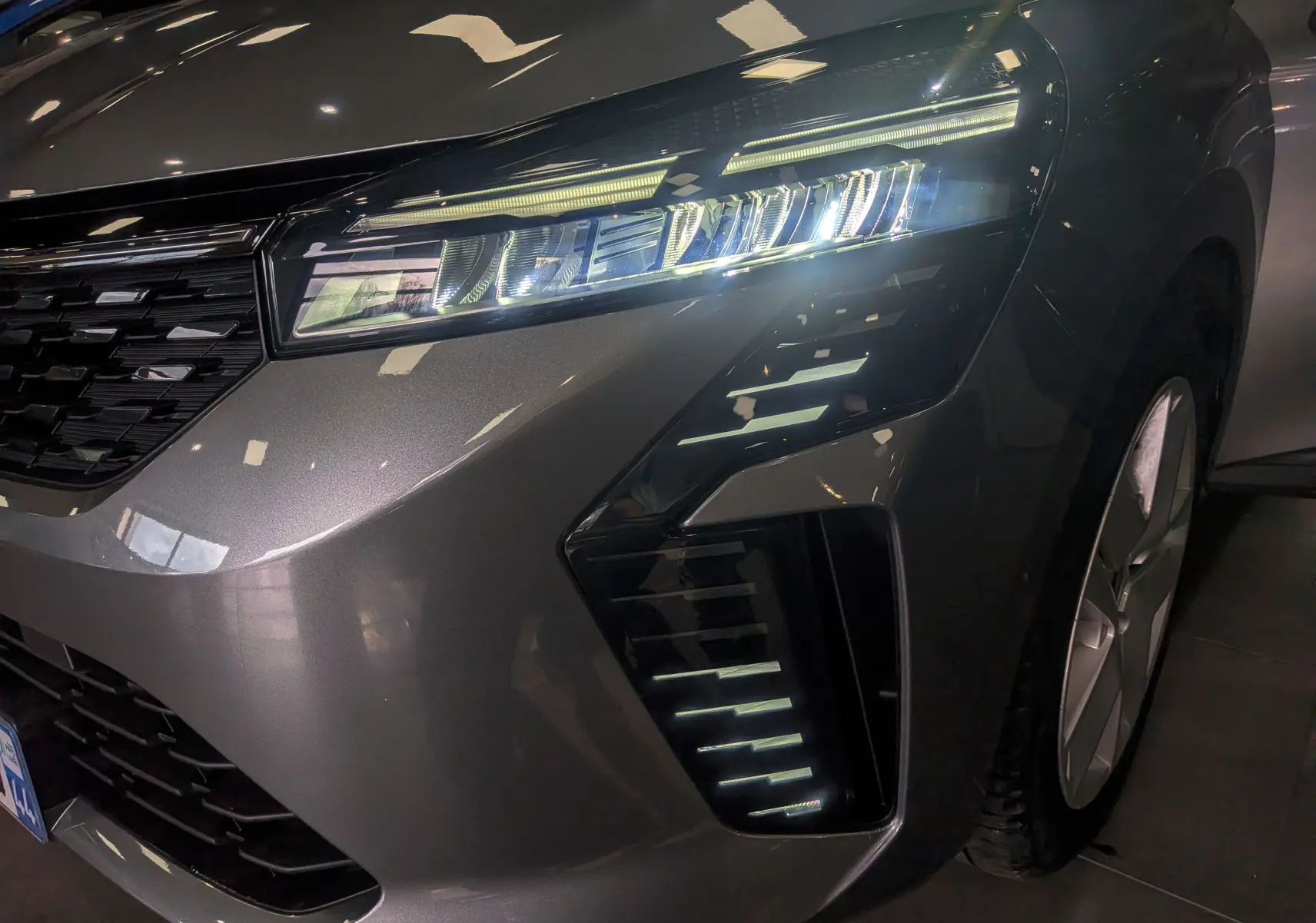 Gros plan sur l'avant droit de la Renault Clio V gris schiste, mettant en valeur son phare LED et la calandre noire brillante.