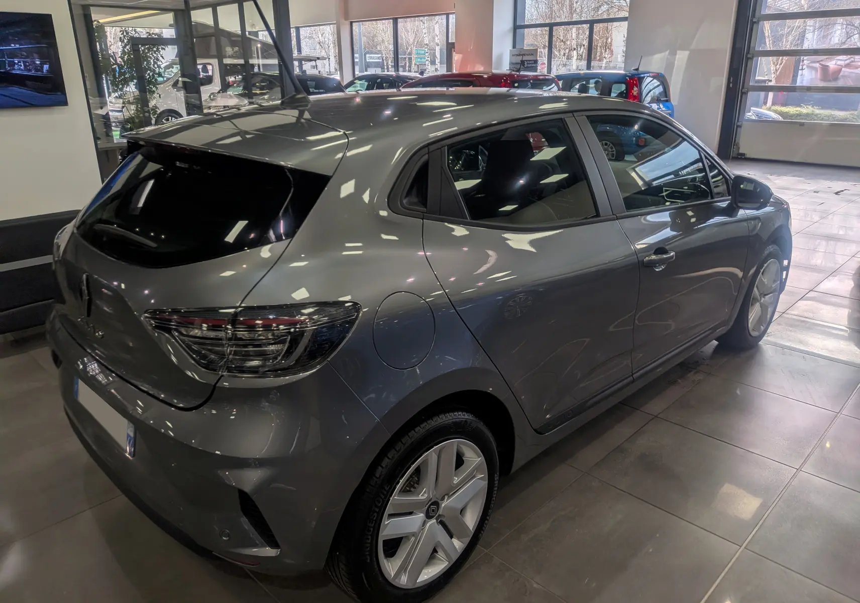 Vue 3/4 arrière droite d'une Renault Clio V TCe 90 Evolution gris schiste en showroom, avec jantes alliage et vitres teintées.