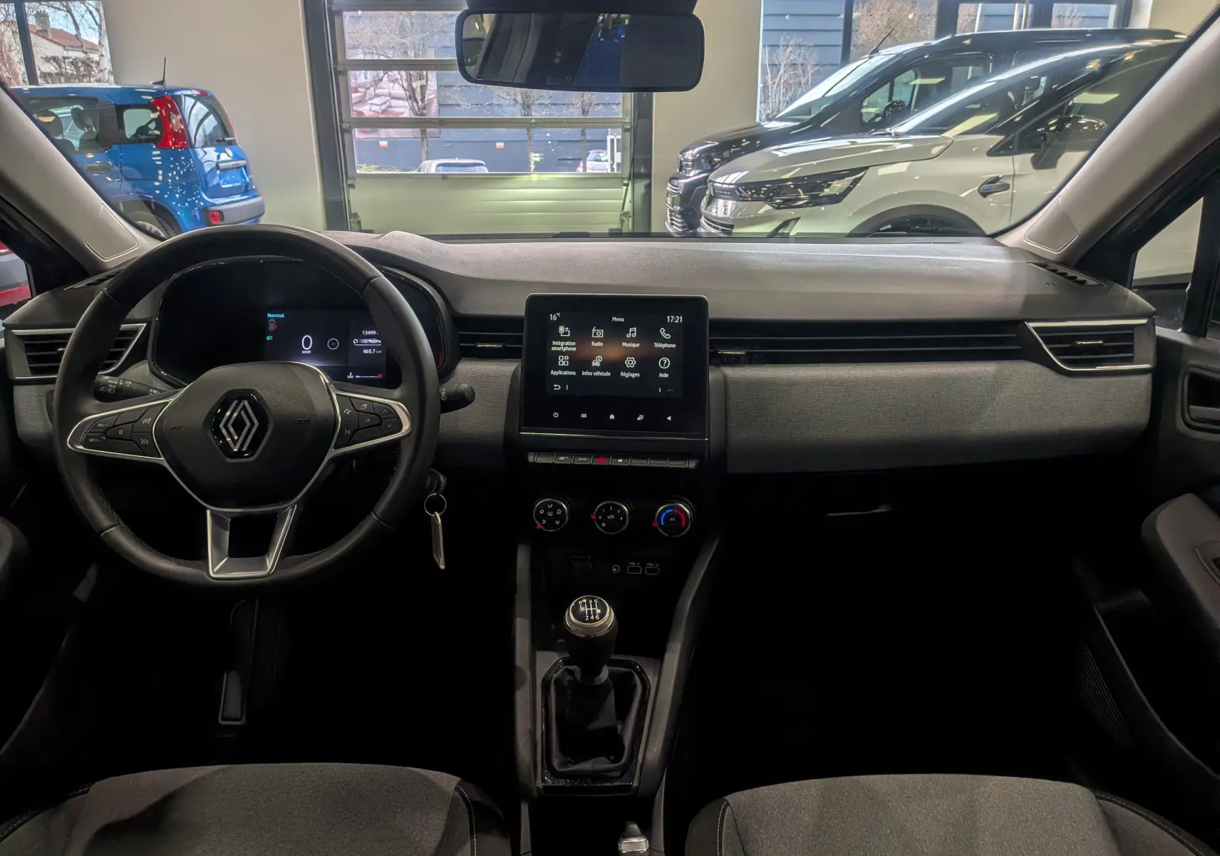 Vue intérieure avant de la Renault Clio V TCe 90 Evolution 2024, tableau de bord gris avec écran tactile et boîte manuelle.