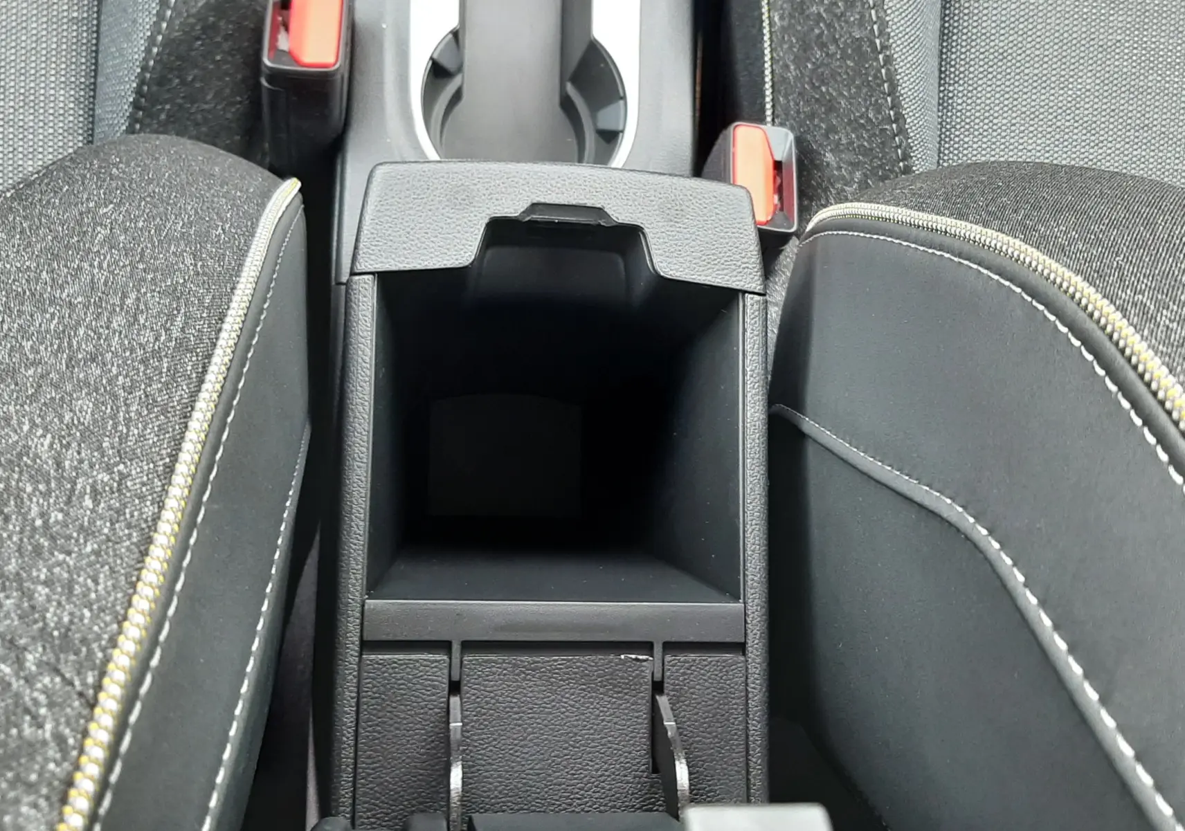 Vue plongeante sur la console centrale ouverte du Renault Captur gris cassiopée avec accoudoirs et porte-gobelets visibles.