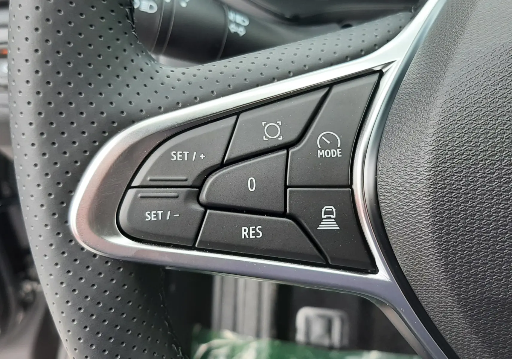 Gros plan sur les commandes à gauche du volant perforé du Renault Captur E-Tech gris cassiopée, boutons de régulateur et mode.