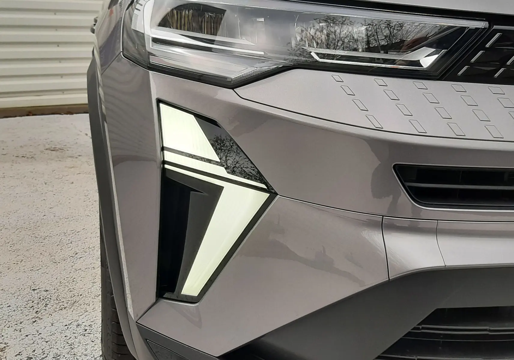 Gros plan sur l'avant gauche du Renault Captur gris Cassiopée, mettant en valeur son phare LED distinctif et la calandre noire.