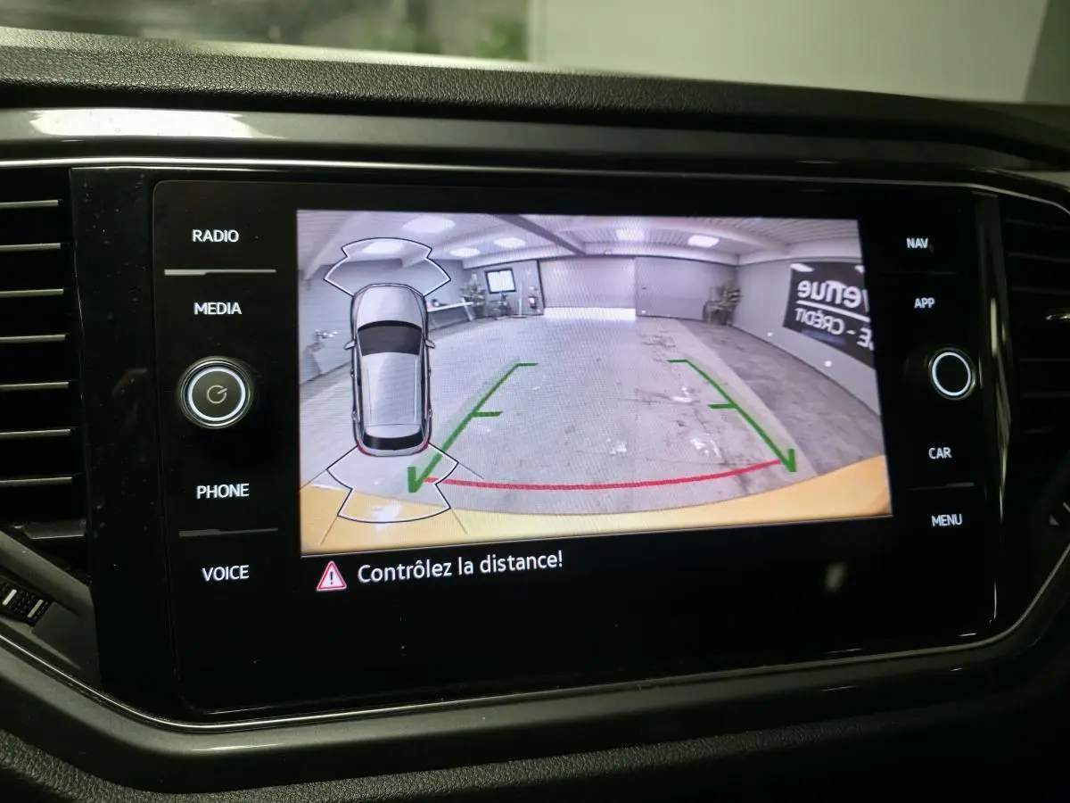 Écran tactile affichant la caméra de recul du Volkswagen T-Roc jaune avec repères de distance et vue aérienne du véhicule.