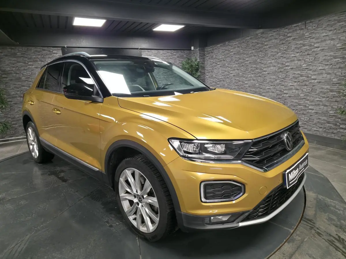 Volkswagen T-Roc jaune vue 3/4 avant droit, avec toit noir et jantes alliage 18 pouces en intérieur showroom.