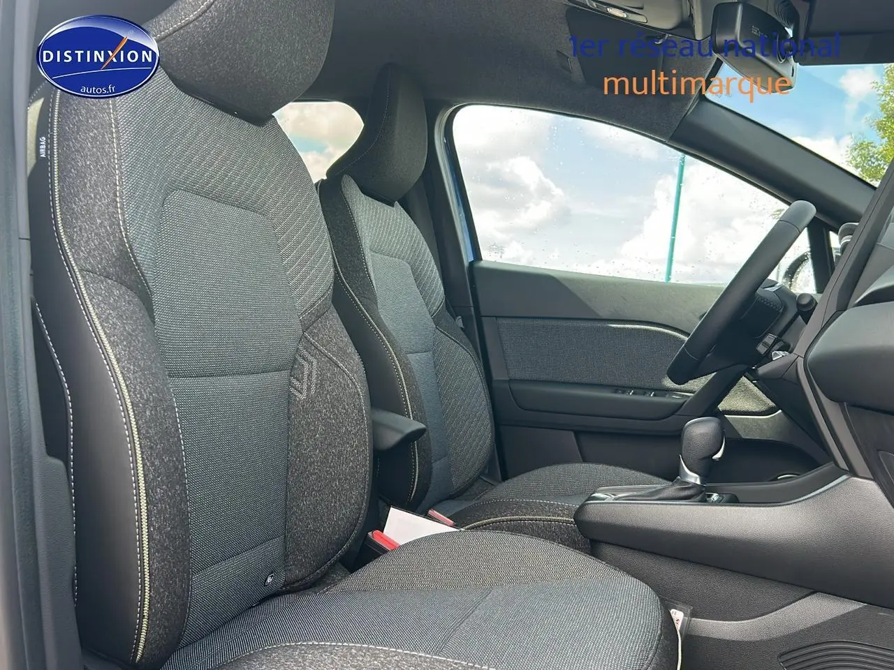 Vue intérieure côté conducteur du Renault Captur 2025, sièges tissu gris avec surpiqûres contrastées et console centrale noire.