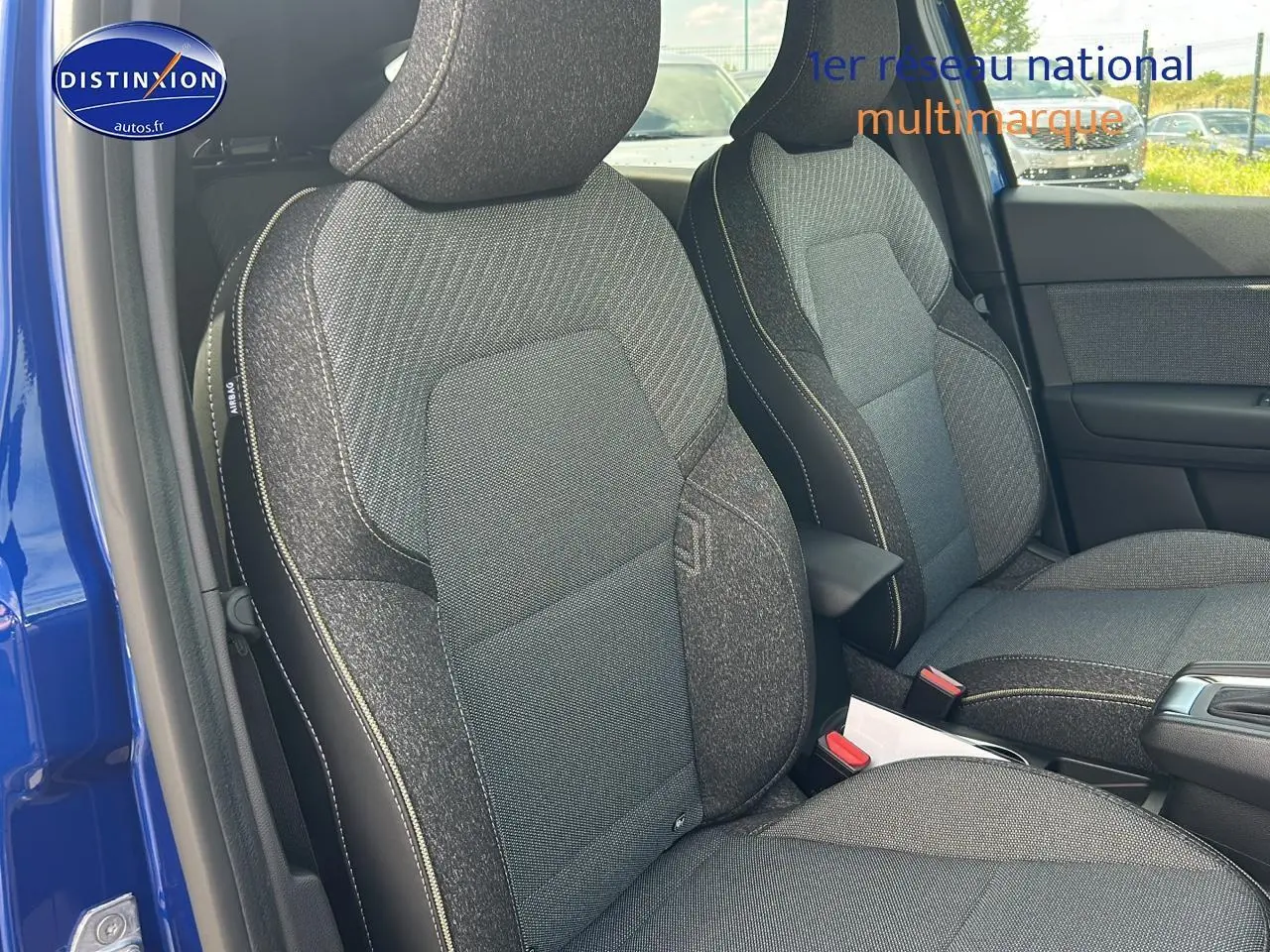Vue intérieure côté conducteur du Renault Captur bleu iron 2025, mettant en valeur les sièges tissu gris et accoudoir central.