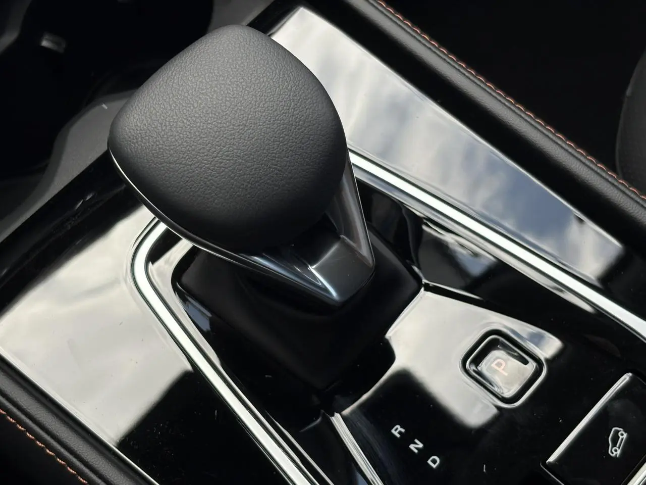 Gros plan sur le levier de vitesses automatique noir brillant de la MG MOTOR EHS 1.5 Hybrid+ 224 Luxury, intérieur noir.