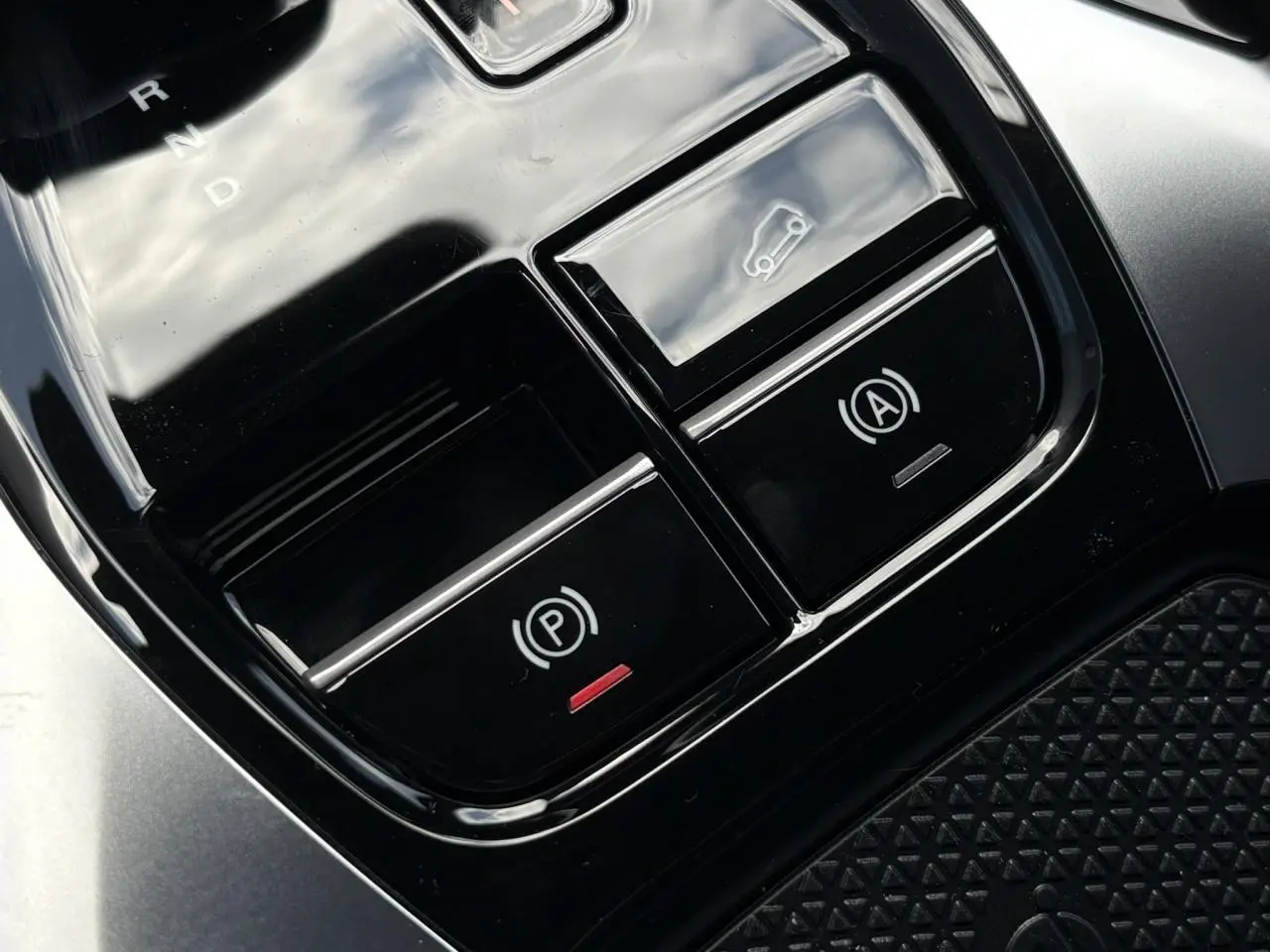 Gros plan sur la console centrale noire avec boutons de frein de stationnement et ouverture du hayon du MG Motor EHS blanc.