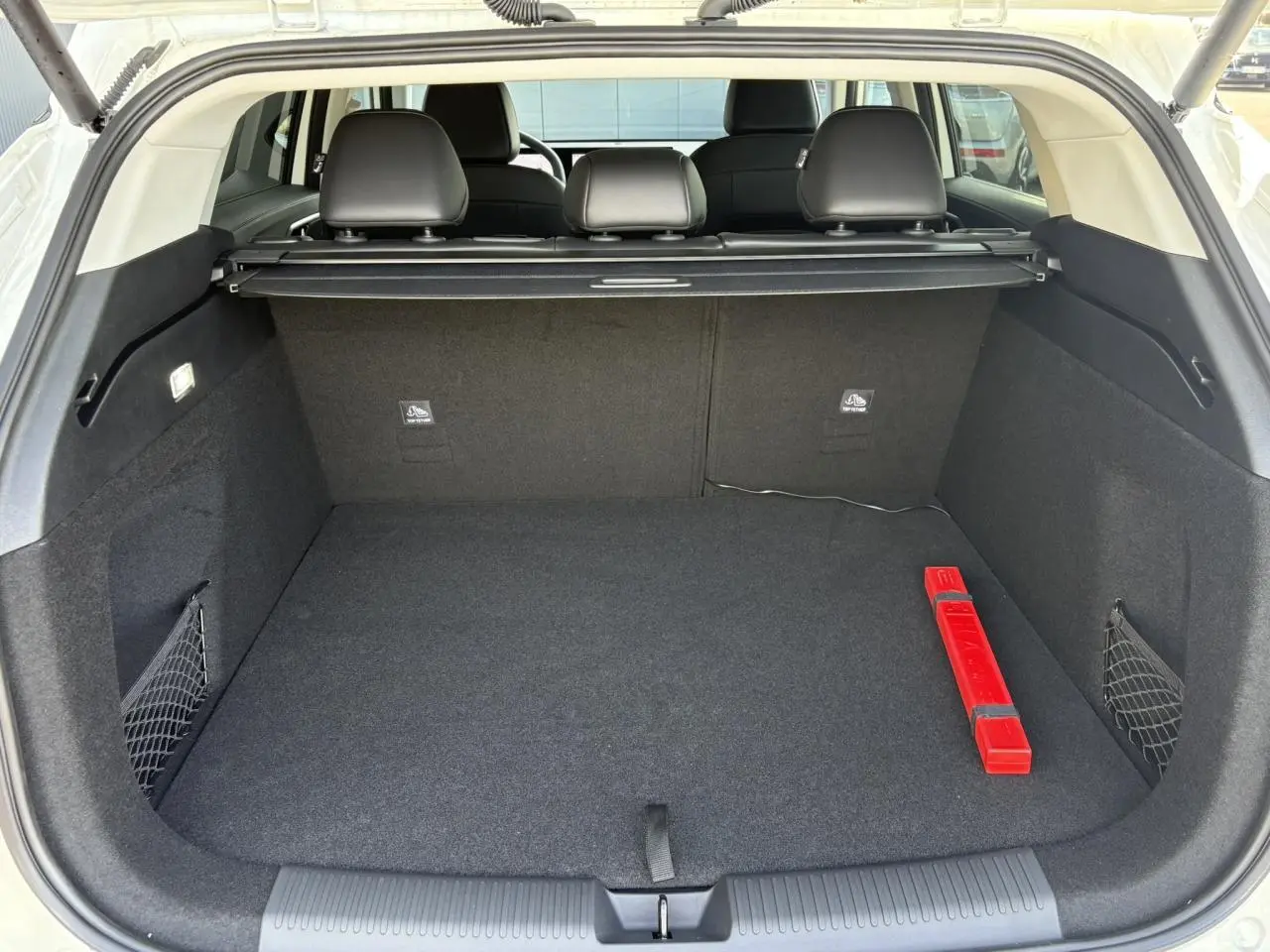 Coffre ouvert d’un MG Motor EHS blanc, vue arrière, avec tapis noir et triangle de signalisation rouge visible.