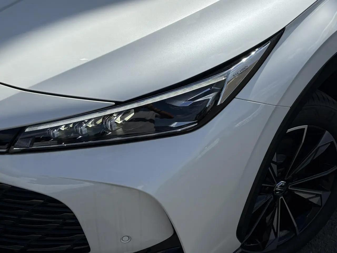 Gros plan sur le phare avant droit et la jante alliage noire du MG Motor EHS blanc métallisé 2026.