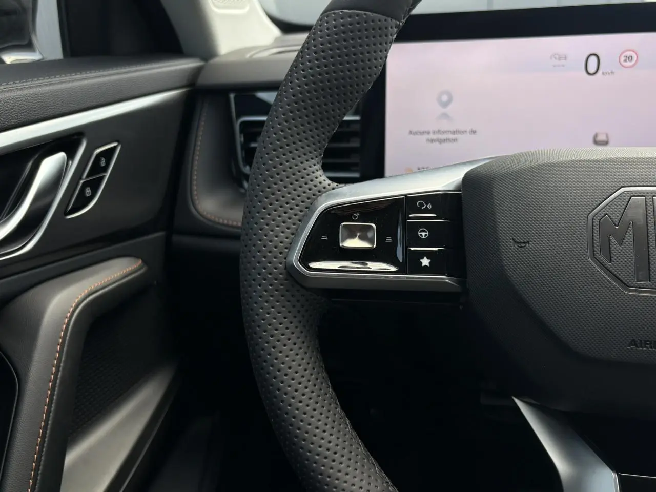 Gros plan sur le volant perforé noir du MG Motor EHS 1.5 Hybrid+ 224 Luxury avec tableau de bord numérique blanc en arrière-plan.