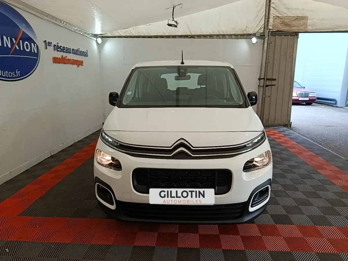 Vue avant d'un Citroën Berlingo blanc 2022 avec calandre noire et phares allumés en intérieur showroom.