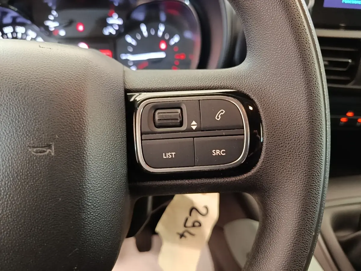 Gros plan sur le volant noir multifonctions du Citroën Berlingo blanc, avec commandes audio et téléphone visibles.