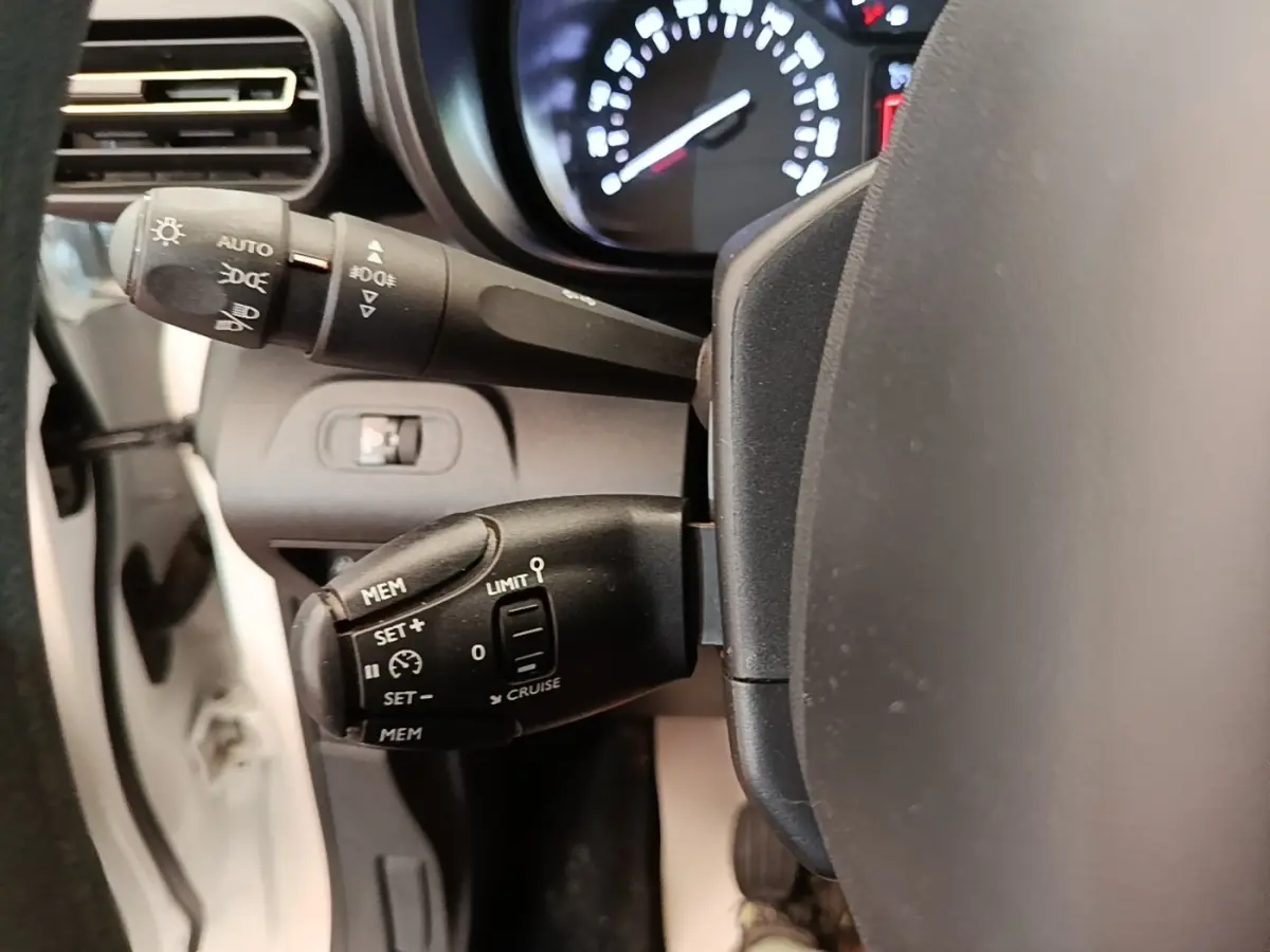 Gros plan sur les commandes de régulateur de vitesse du volant d'une Citroën Berlingo blanc, tableau de bord flou en arrière-plan.