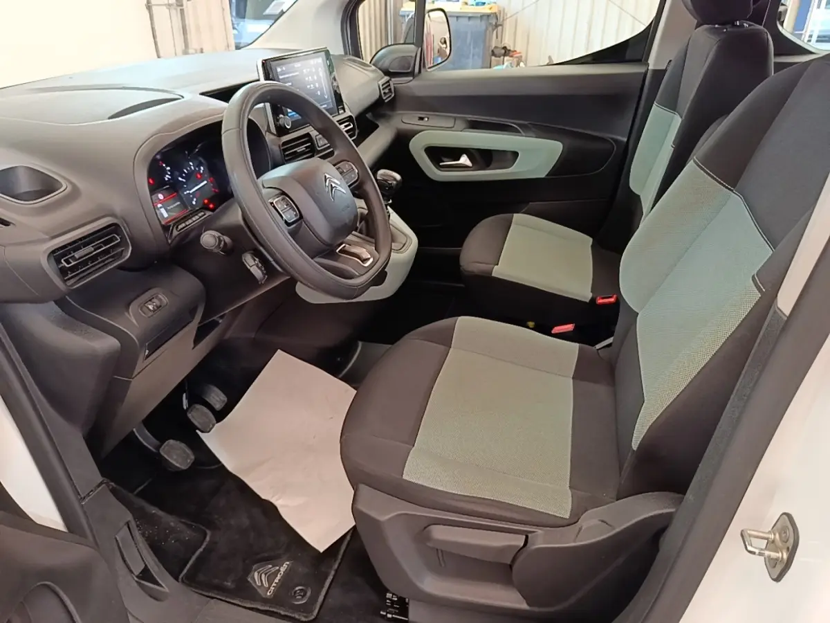 Vue intérieure côté conducteur du Citroën Berlingo blanc, montrant le volant multifonctions et les sièges bi-ton gris et noir.