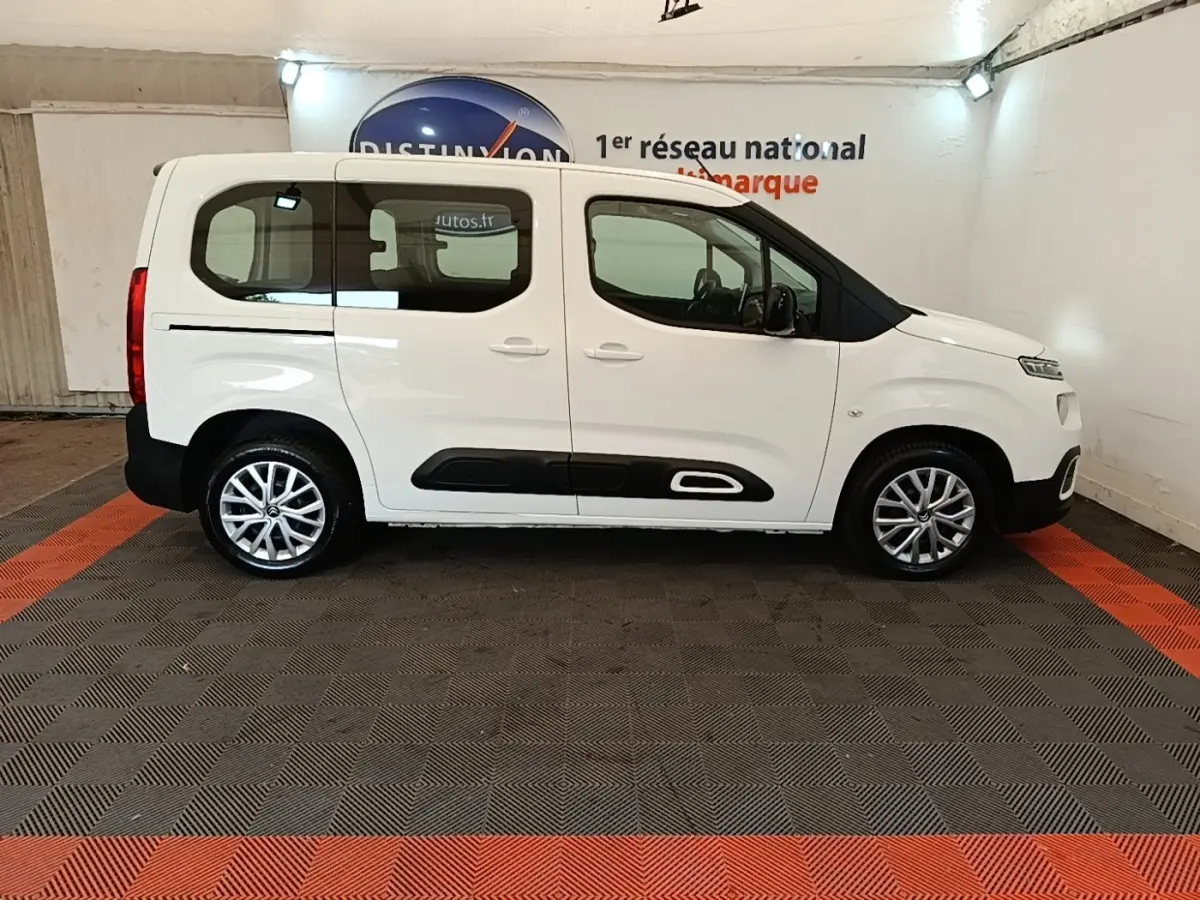Profil droit d'un Citroën Berlingo blanc 2022 avec protections noires basses et jantes alliage en intérieur showroom.